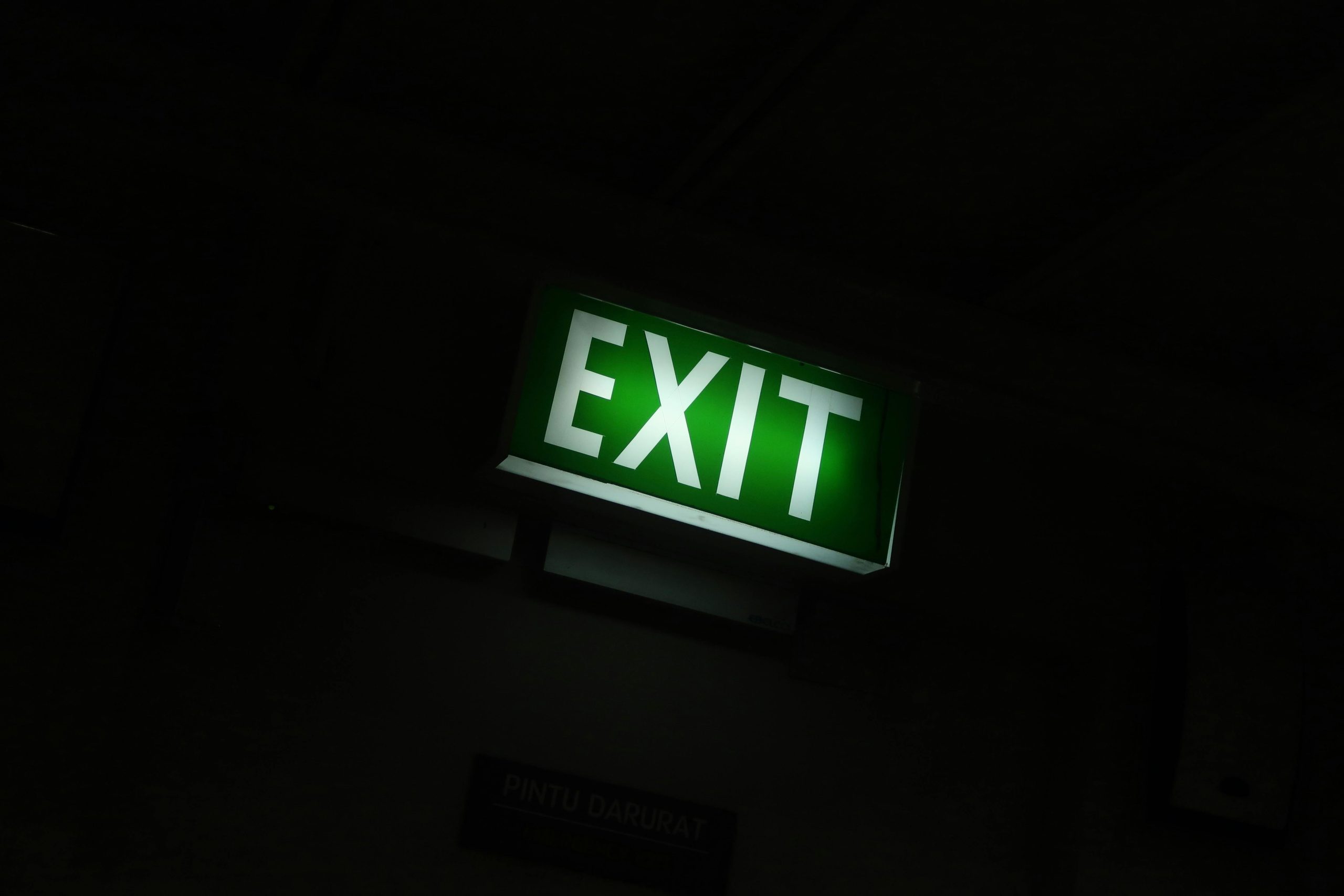 A glowing green exit sign provides guidance in a dimly lit indoor space.
